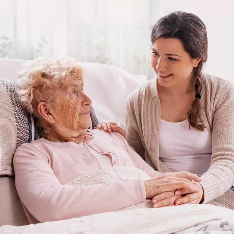Eine junge Frau hält einer älteren Frau in der Palliativversorgung die Hand