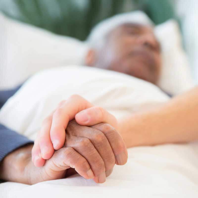Älterer Mann in der Palliativversorgung liegt im Bett und wird von Angehörigen begleitet